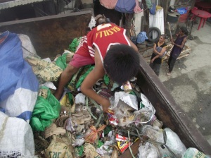 One orphaned child in a squatter area scavenging inside a truck through the garbage we threw away